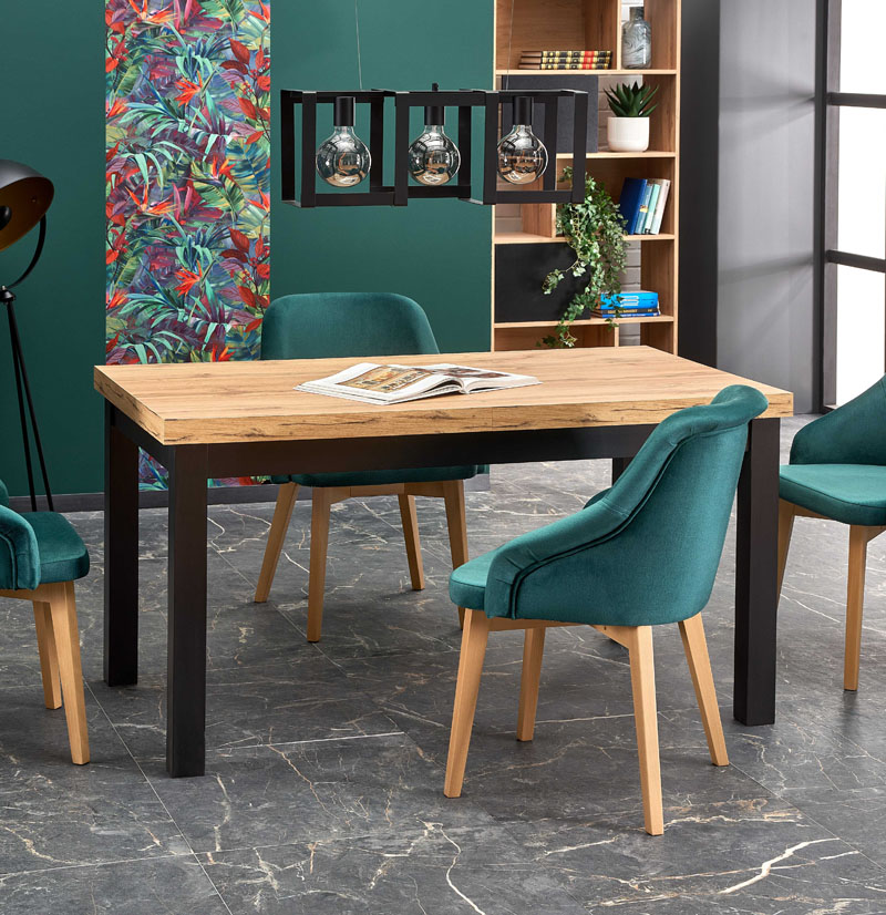 Stół rozkładany Tiago 140 z blatem w kolorze dąb craft oraz ramą i nogami w kolorze czarnym, w pomieszczeniu w stylu eklektycznym z zielonymi ścianami oraz kamienną podłogą. Przykładowa prezentacja z oferty sklepu producenta stołów.